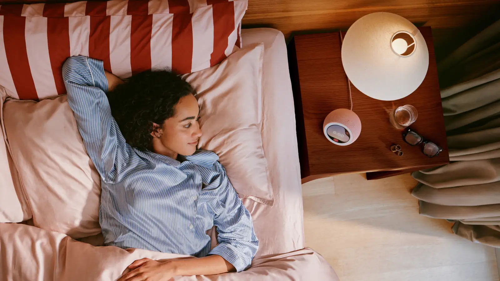 Mujer acostada en la cama junto a un Amazon Echo Time sobre la mesa de luz