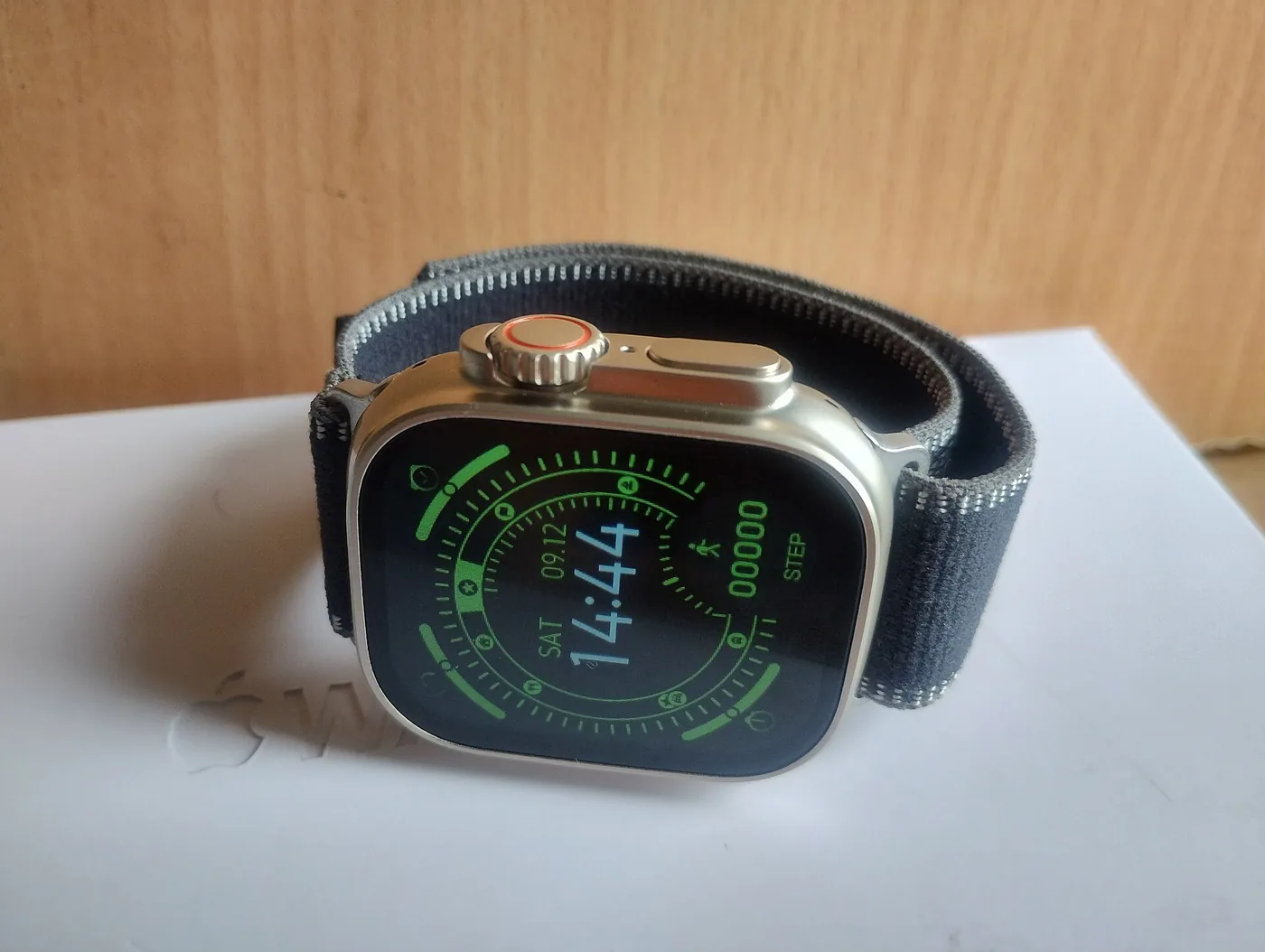 Apple Watch Ultra 3 de titanio con malla Ocean, apoyado de costado sobre su caja