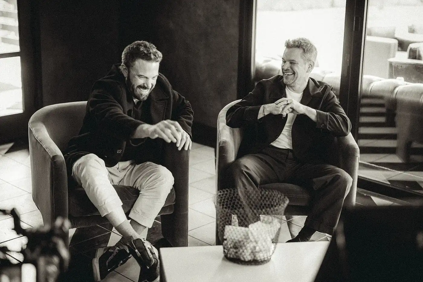 Ben Affleck y Matt Damon se ríen sentados en sillones durante la prensa de Air en Austin, en blanco y negro