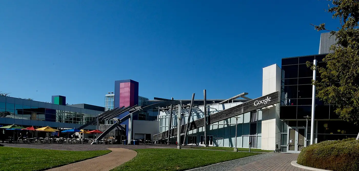 Vista del campus de Google en Mountain View, con edificios de vidrio, jardines y un cielo despejado