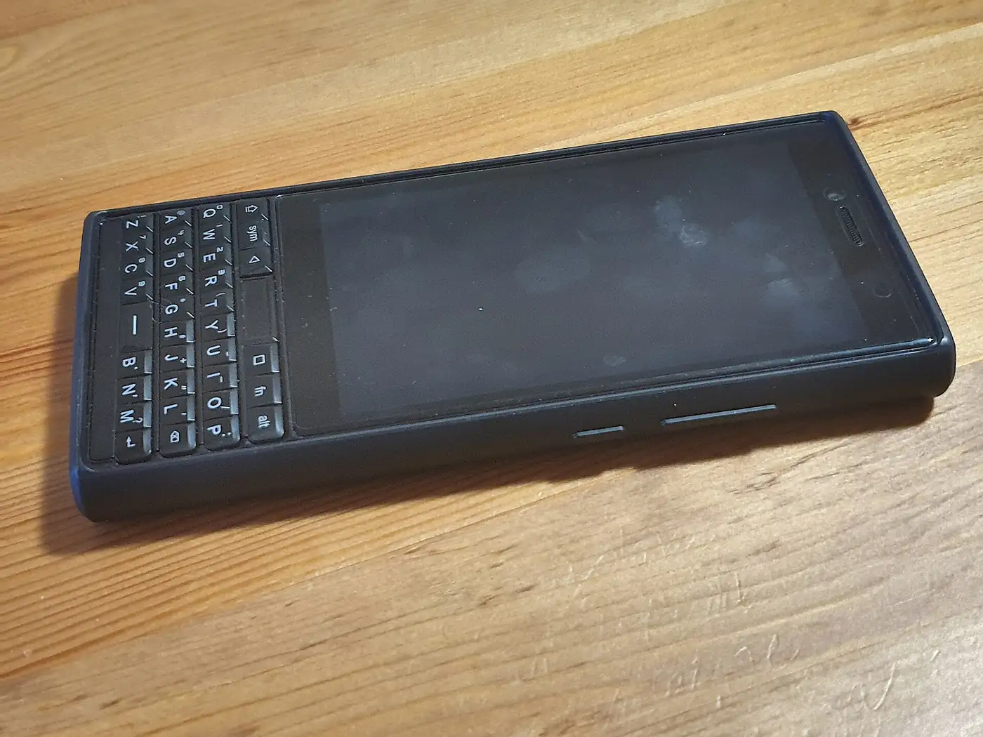 Celular Unihertz Titan Slim con teclado físico, usado como teléfono accesible, apoyado sobre una mesa de madera