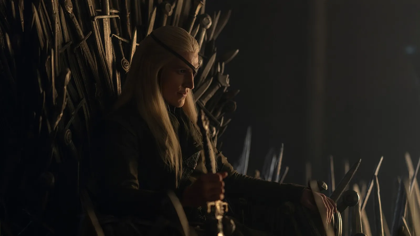Ewan Mitchell como Aemond Targaryen, con el parche en el ojo, sentado en el Trono de Hierro en la temporada 3 de House of the Dragon