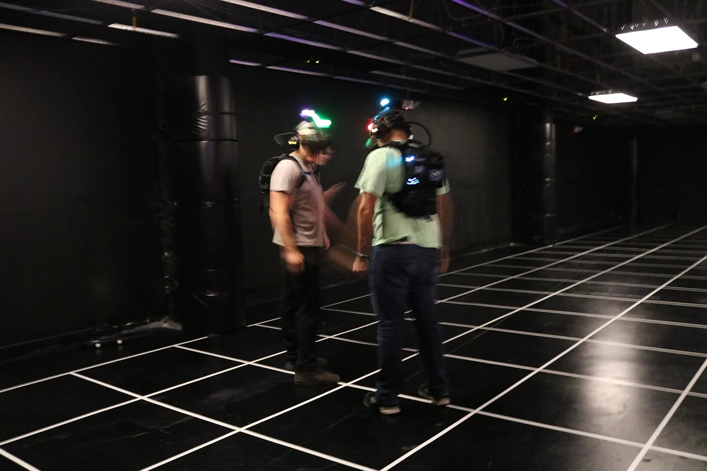 Dos personas con cascos de realidad virtual y mochilas recorren un espacio de juego inmersivo