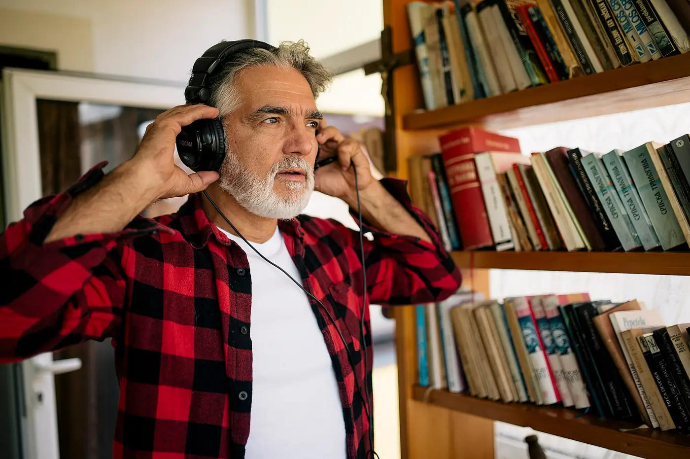 Hombre mayor escucha música con auriculares junto a una biblioteca