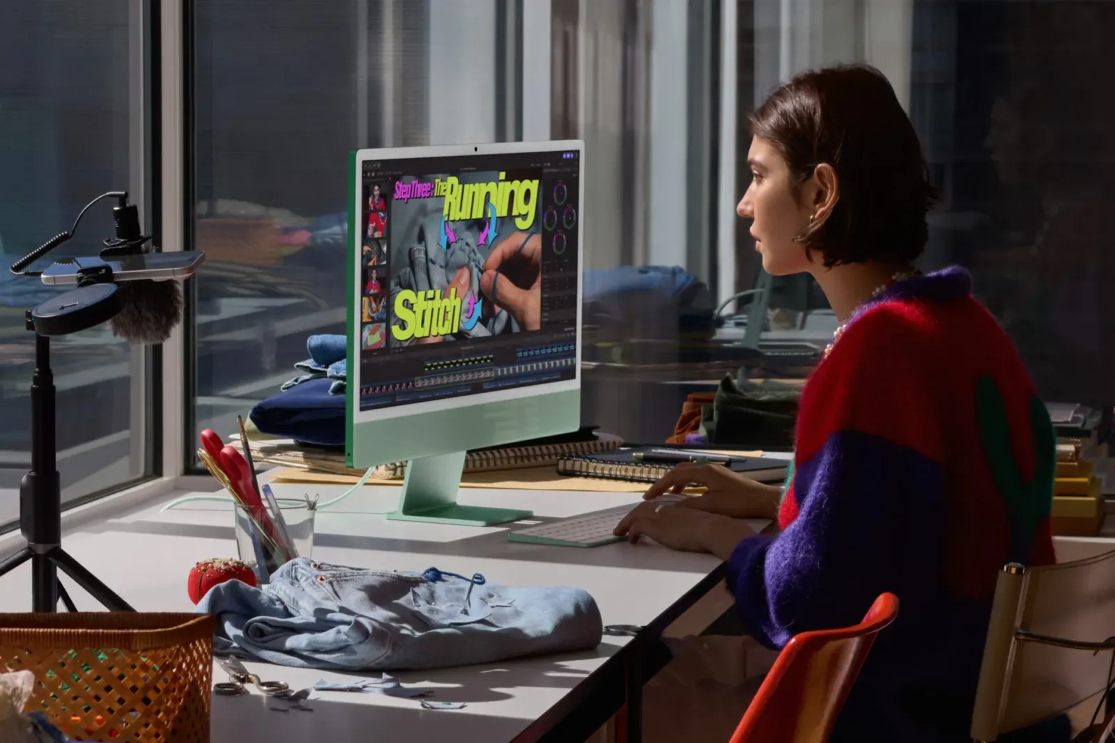 Una mujer edita un video en la nueva iMac con M6 verde, en un escritorio junto a la ventana