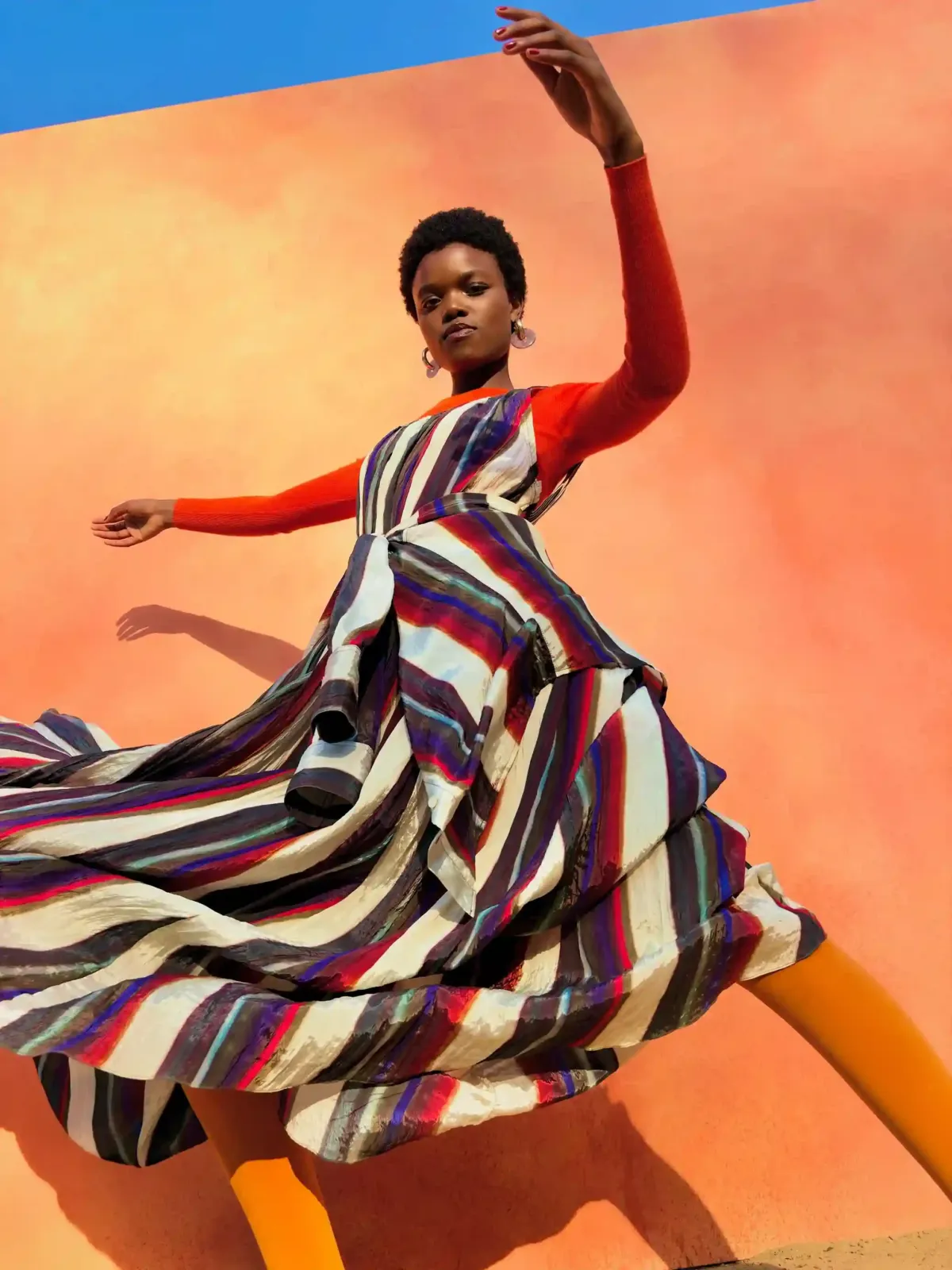 Foto de muestra del iPhone Duo: una mujer baila con un vestido a rayas frente a una pared naranja
