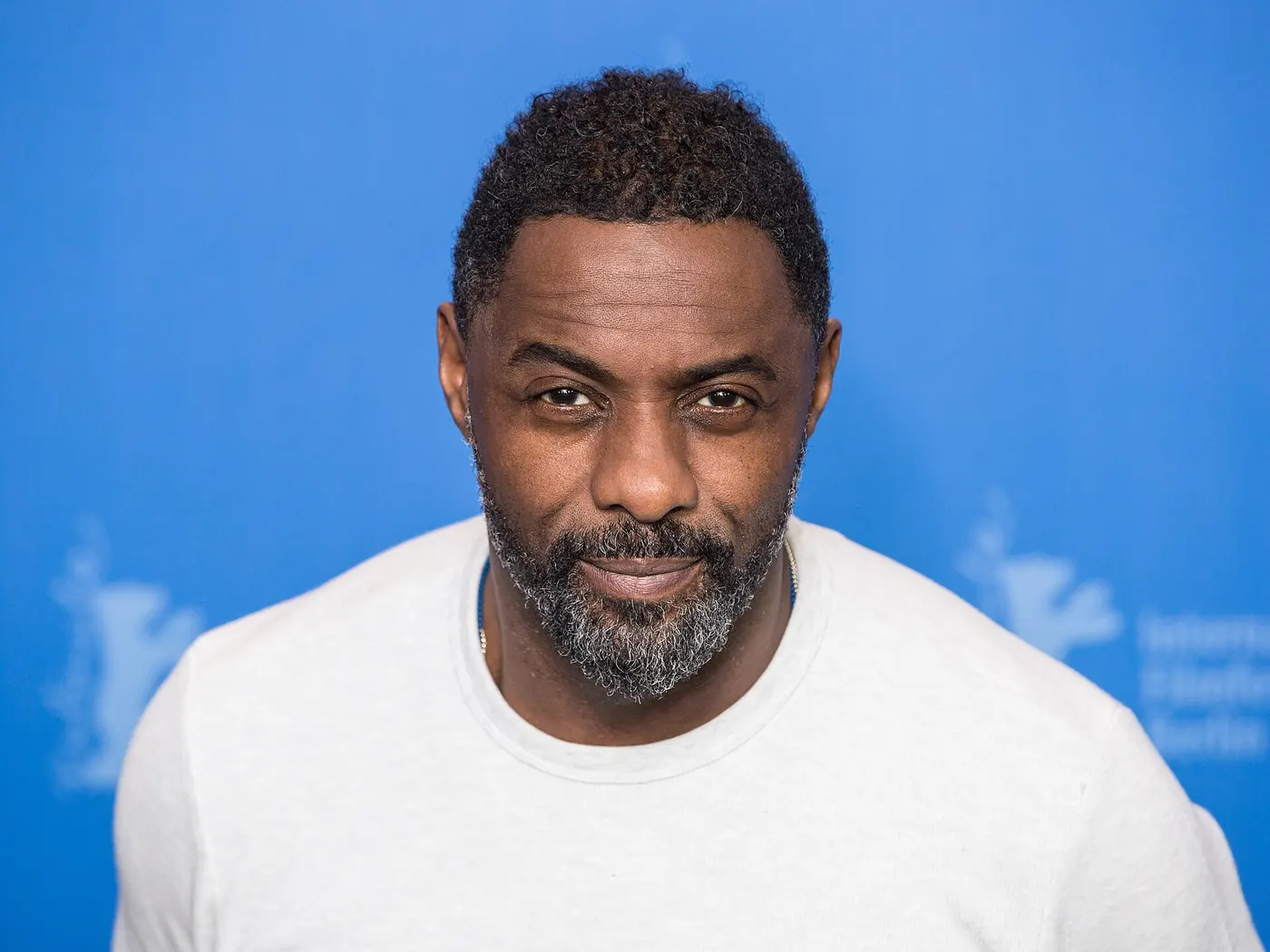 Retrato de Idris Elba con remera blanca frente a un fondo azul en la Berlinale
