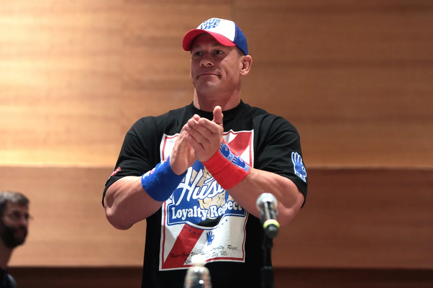 John Cena, protagonista de Peacemaker, aplaude parado frente a un micrófono en una convención