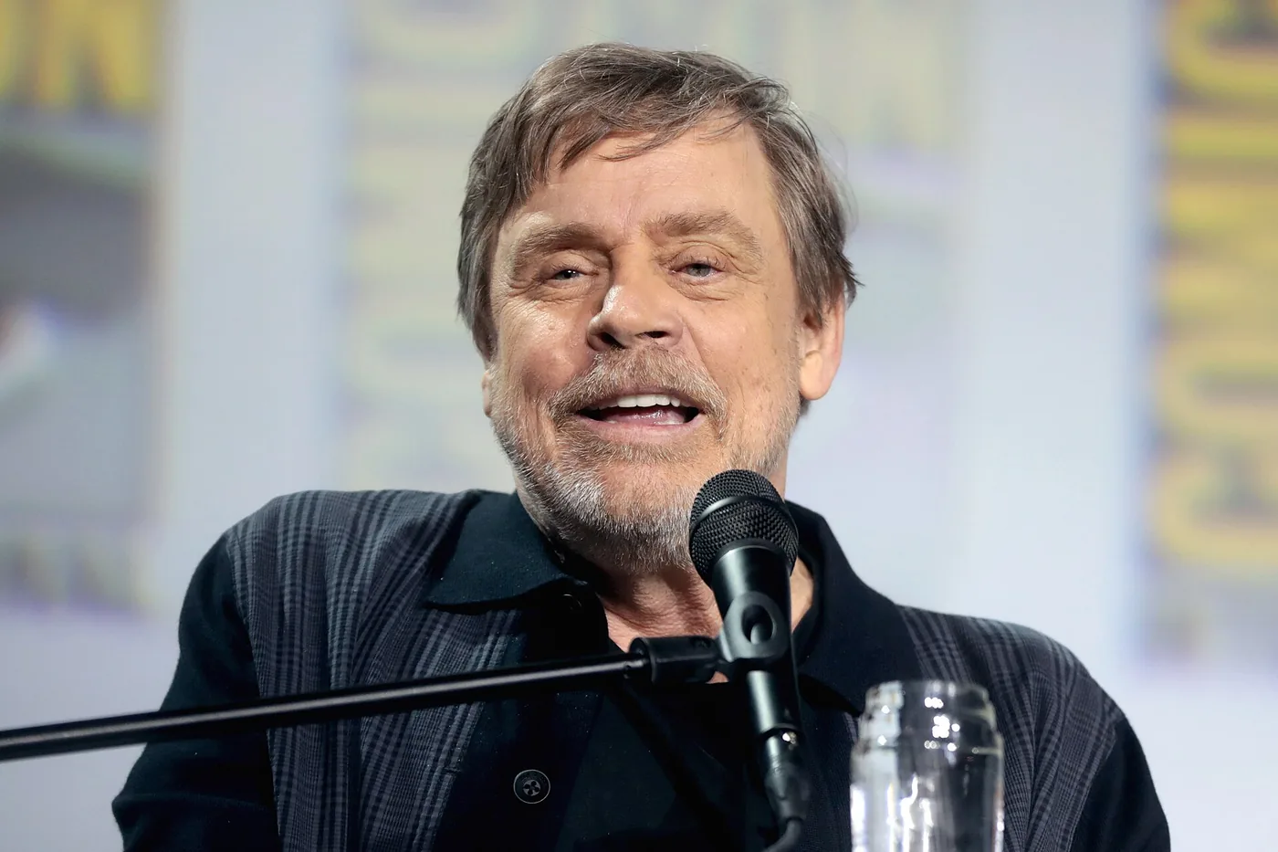 Mark Hamill sonríe y habla frente a un micrófono en un panel de la Comic-Con de San Diego