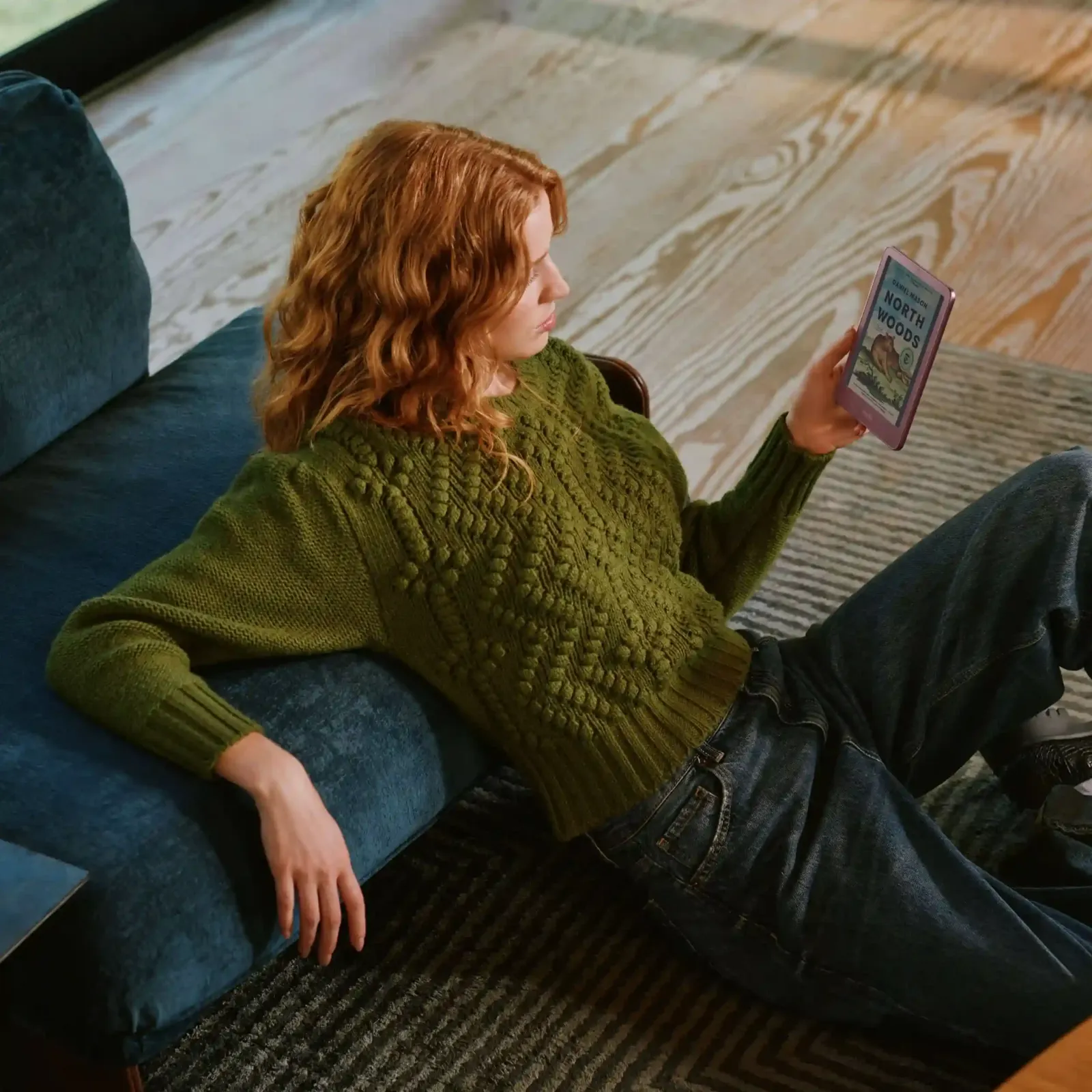 Una mujer lee en un nuevo Kindle de Amazon, sentada en el piso junto a un sillón