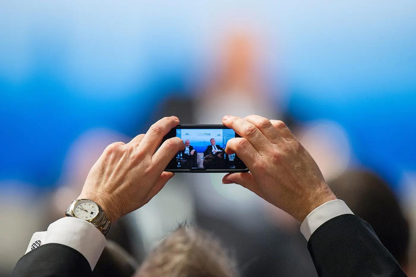 Una persona sostiene un smartphone con las dos manos para sacar una foto entre el público