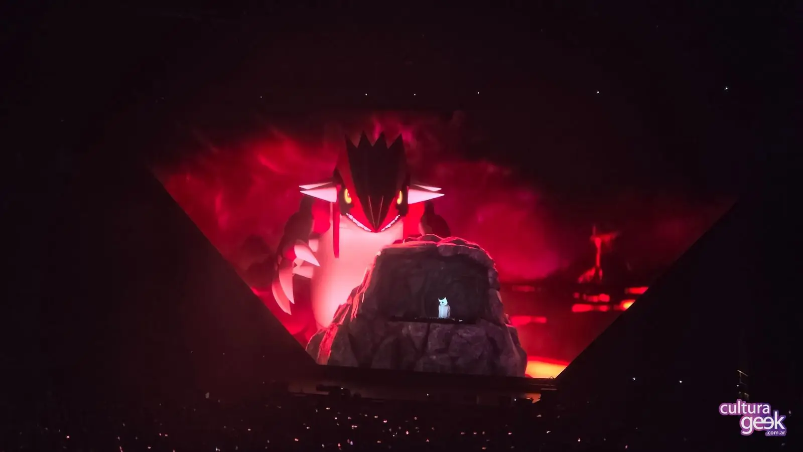 Groudon gigante en la pantalla triangular de Pokémon Night Out 2026, con Marshmello pasando música en una cabina con forma de roca en el Intuit Dome