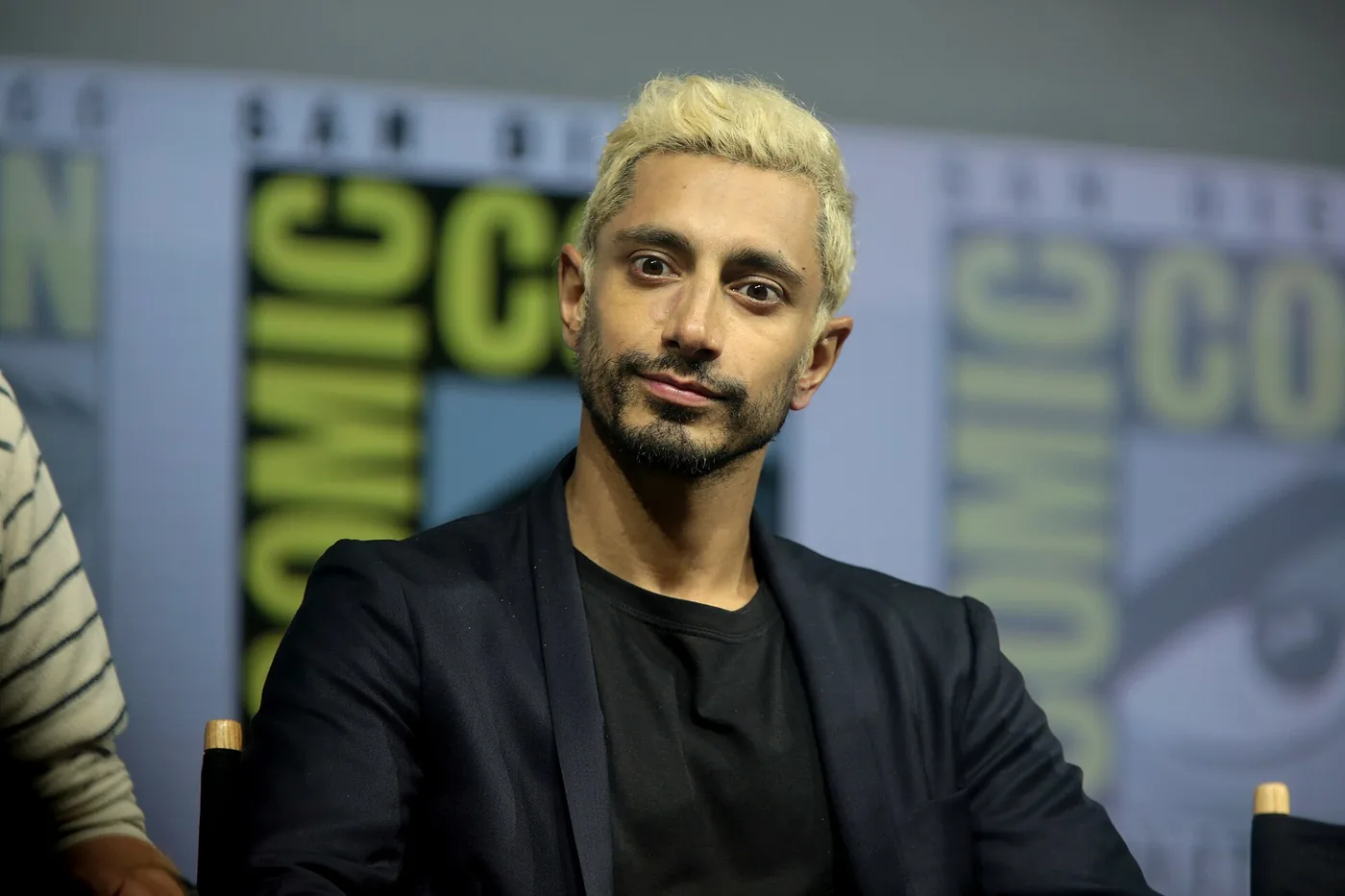 Riz Ahmed, con el pelo teñido de rubio, sentado en un panel de la Comic-Con de San Diego