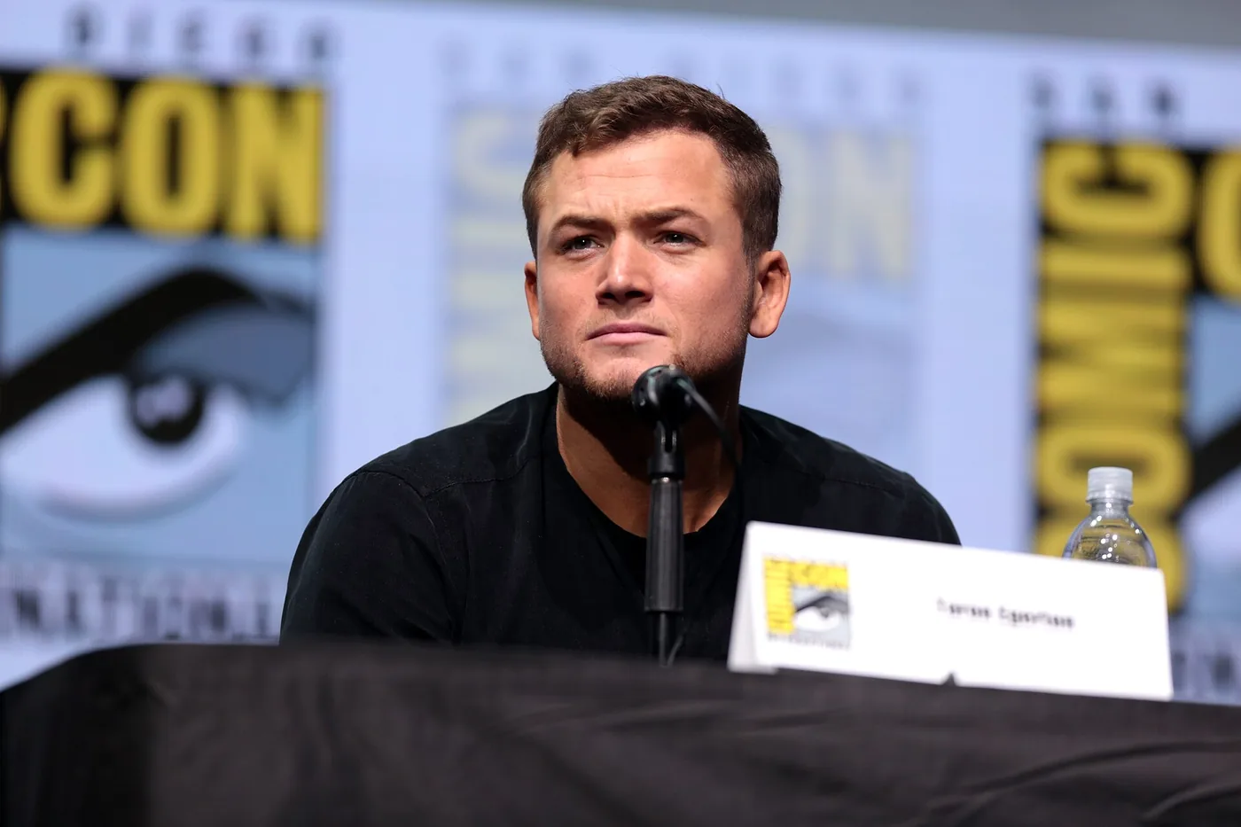 Taron Egerton sentado frente a un micrófono en un panel de la Comic-Con de San Diego