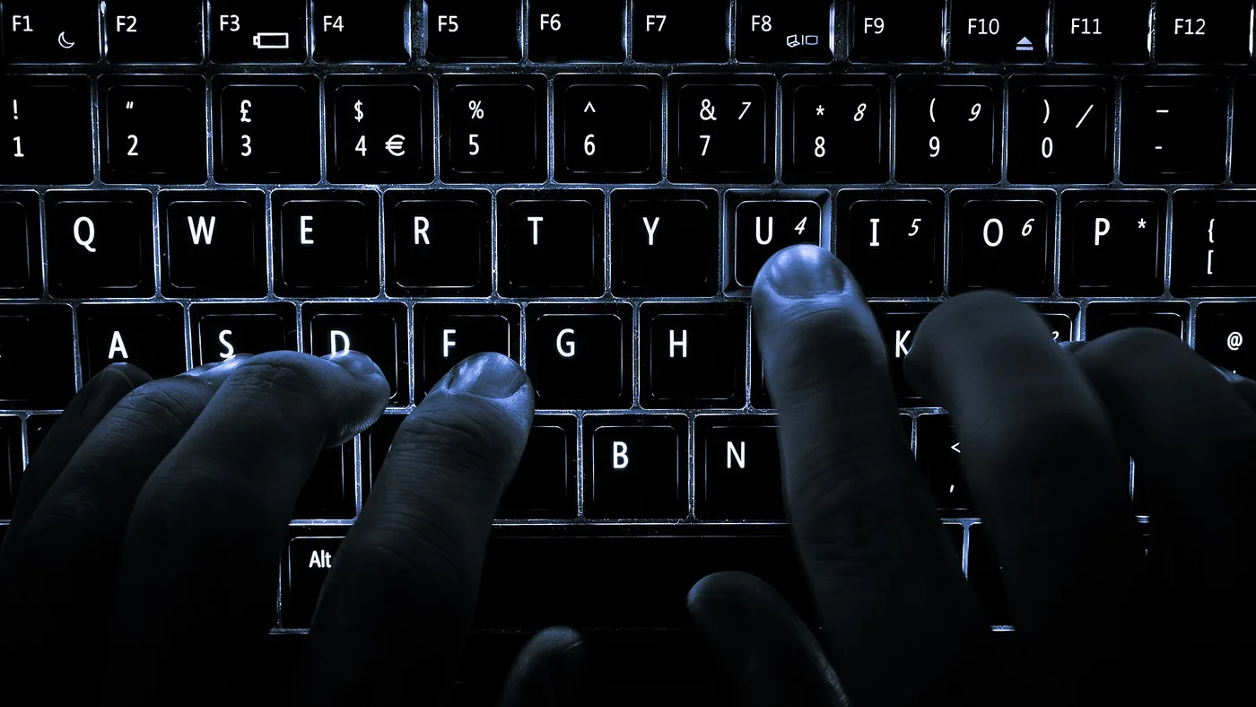 Manos escribiendo en el teclado retroiluminado de una notebook en la oscuridad