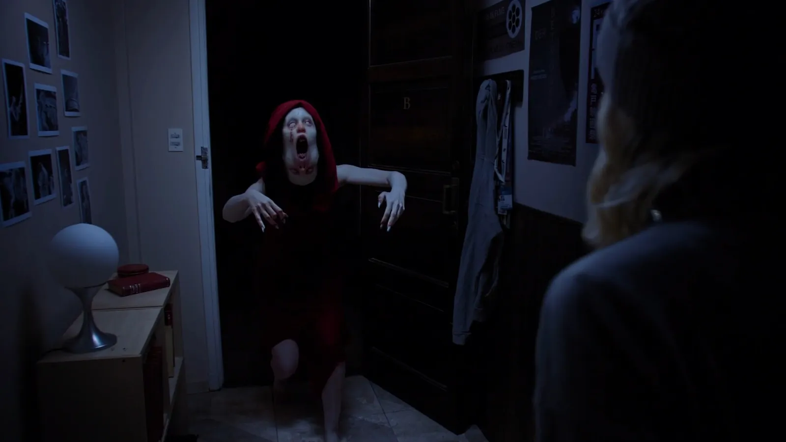 Escena live-action de Tenebris Somnia: una criatura con capucha roja se abalanza sobre la protagonista en un departamento a oscuras