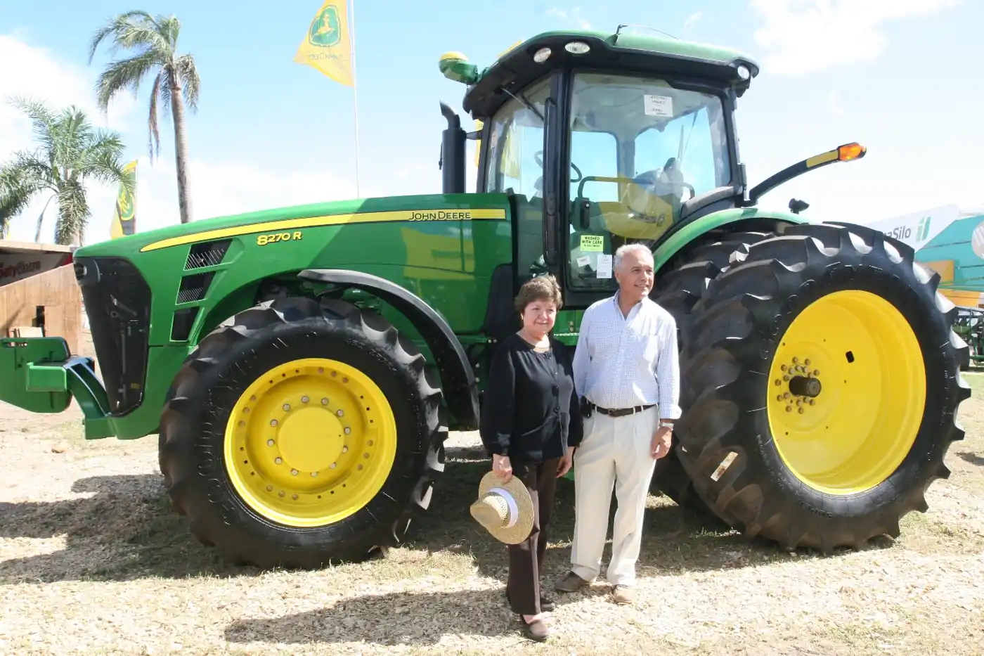 Tractor John Deere 8270R exhibido en una muestra agrícola en Argentina, con dos visitantes posando al lado
