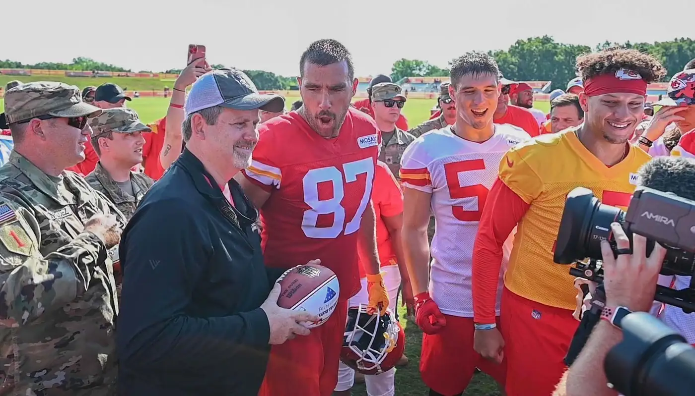 Travis Kelce, con la camiseta 87 de los Kansas City Chiefs, rodeado de militares y compañeros en el campo de entrenamiento de 2022